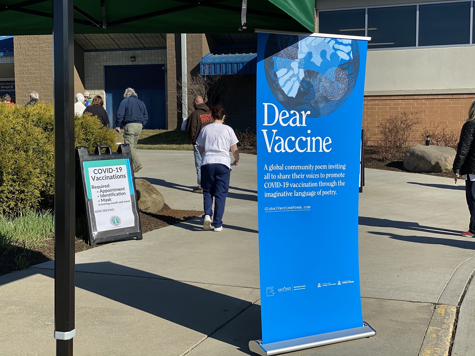 A banner promoting the Global Vaccine Poem project stands outside the Kent State University Field House during a mass COVID-19 vaccination event.