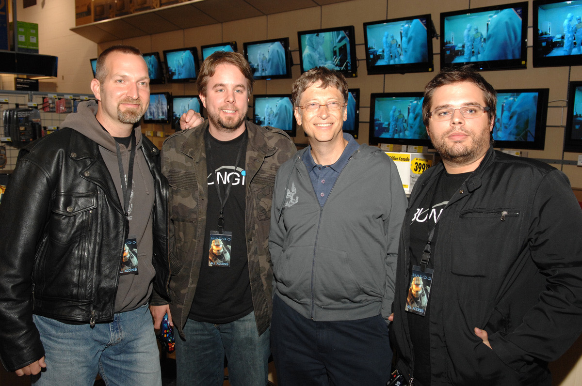 Marcus Lehto standing with Bill Gates and two other Bungie team members in front of a wall of Halo 3 demo screens.