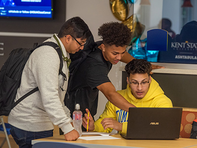 Photo of students, gathered together working on a laptop