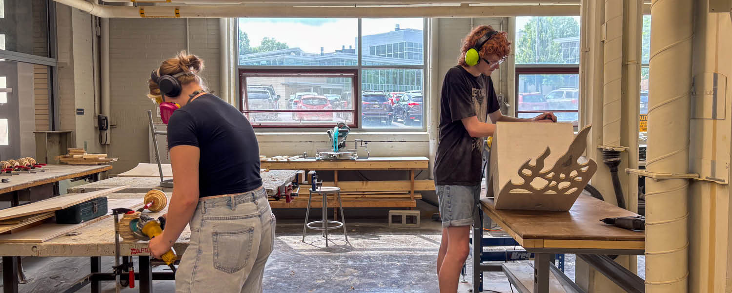 Artists use woodworking tools to carve sculptures in a studio space