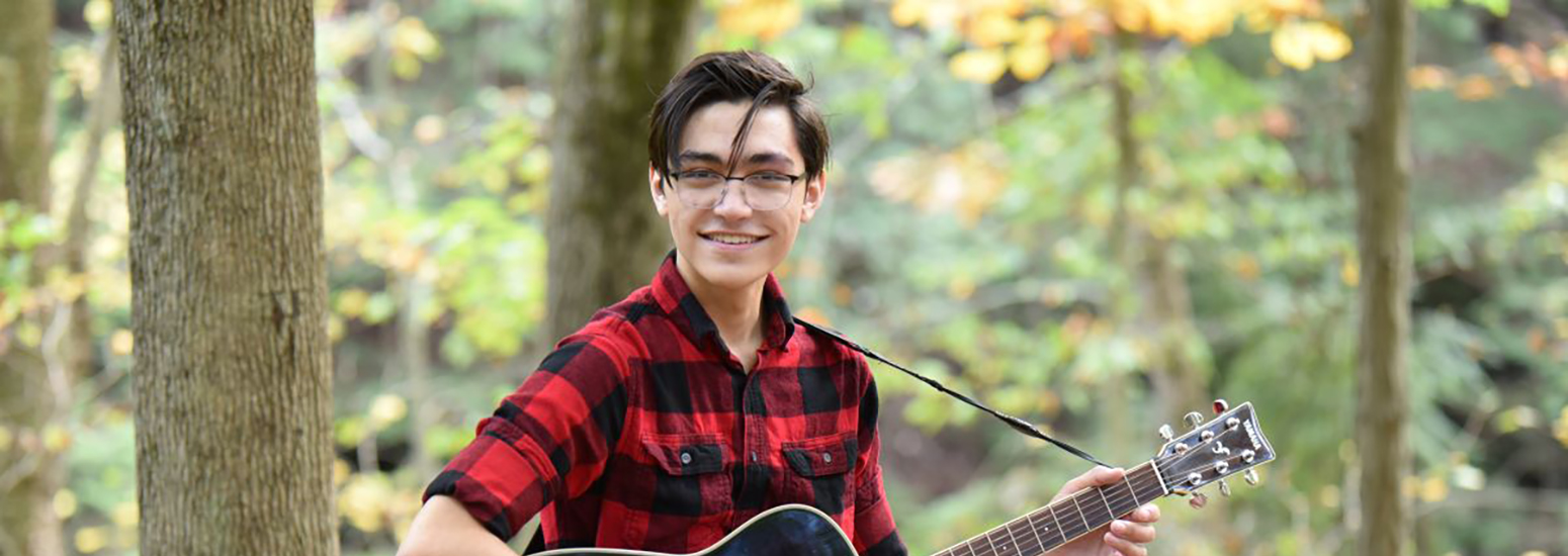 Honors College student Daniel Zalamea poses in the woods with his guitar