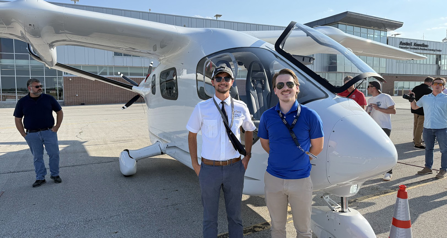 Two student pilots stand next to a modern single-engine aircraft outdoors.