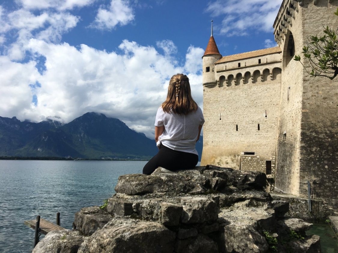 Student in Switzerland sitting next to a castle overlooking a lake.