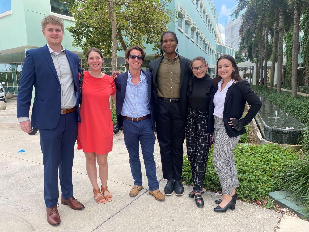 Students posing for a group photo in the Cayman Islands. There is greenery and a mint colored building in the background.