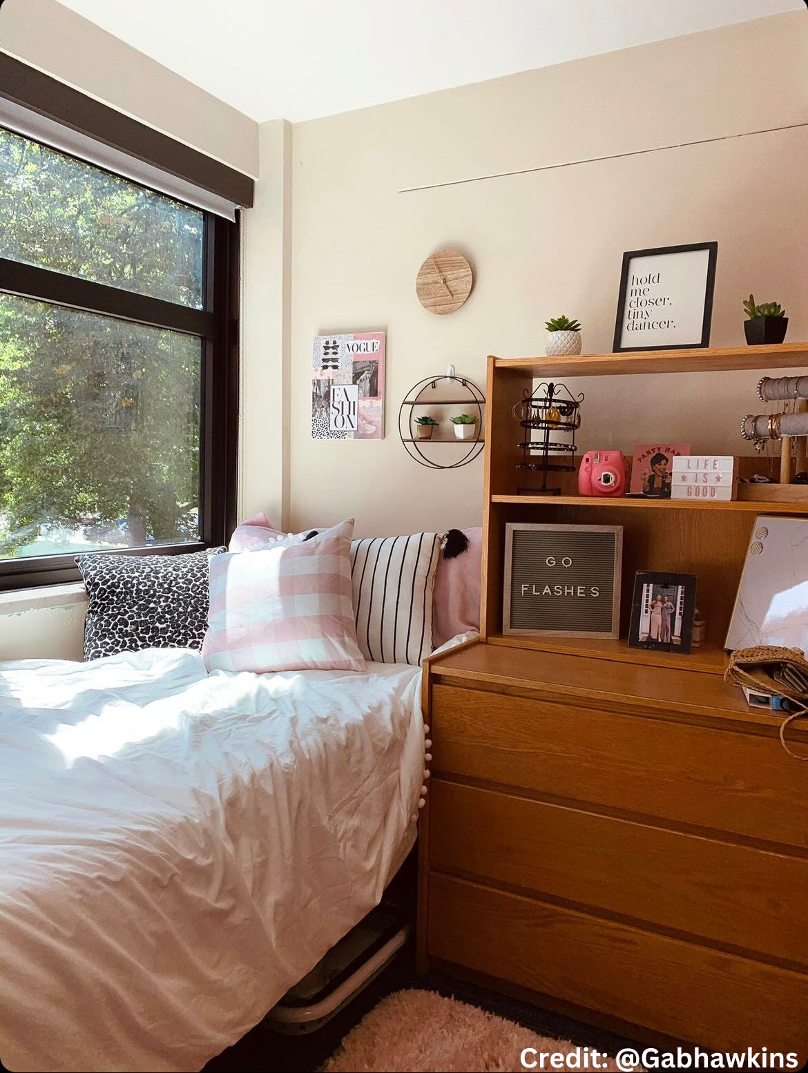 A dorm room with pink decorations and pink and white pillows.