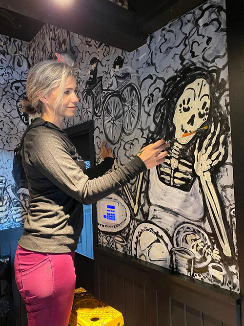 Eileen Dorsey painting an indoor mural of a skeleton for the restaurant Barrio