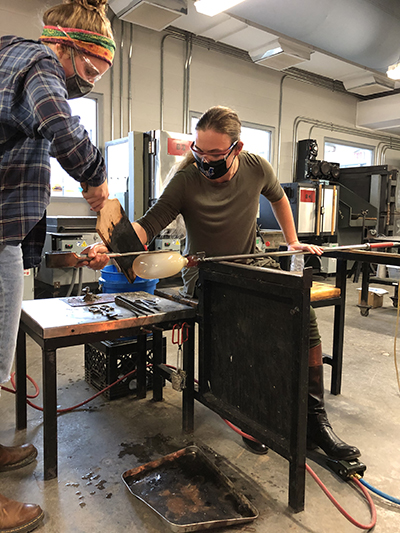 Glass students using the foot pedal with face coverings on to blow glass