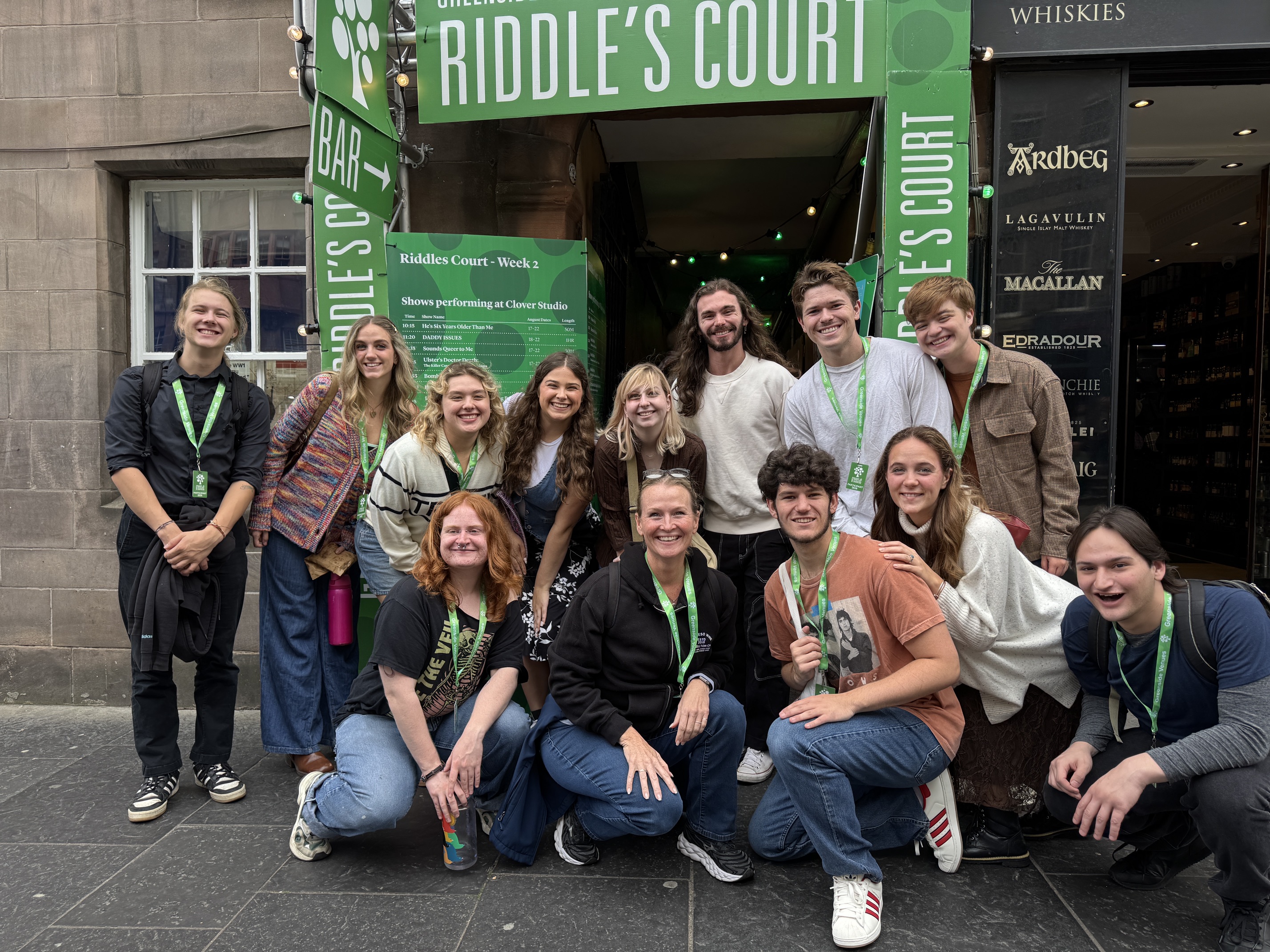 A group shot of participants posing in front of a green sign, many wearing green necklaces