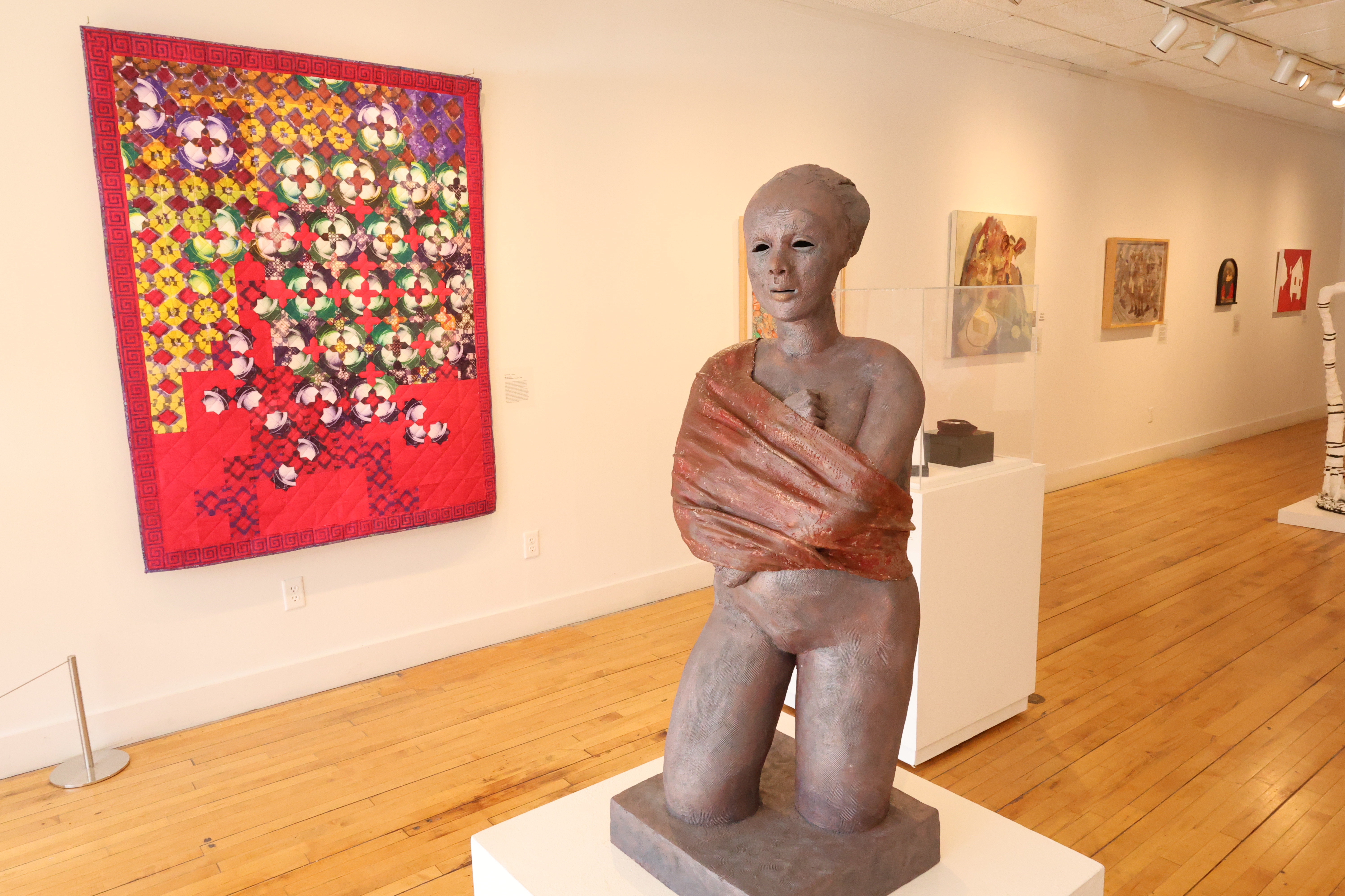 Sculpture in the center of an art gallery with artwork hanging on the wall behind