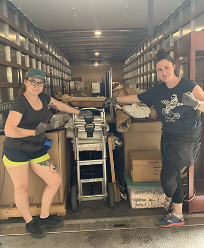 Fran Ugalde Z. at her job loading a truck. Two women in front of a loaded truck bed with clenched fists.