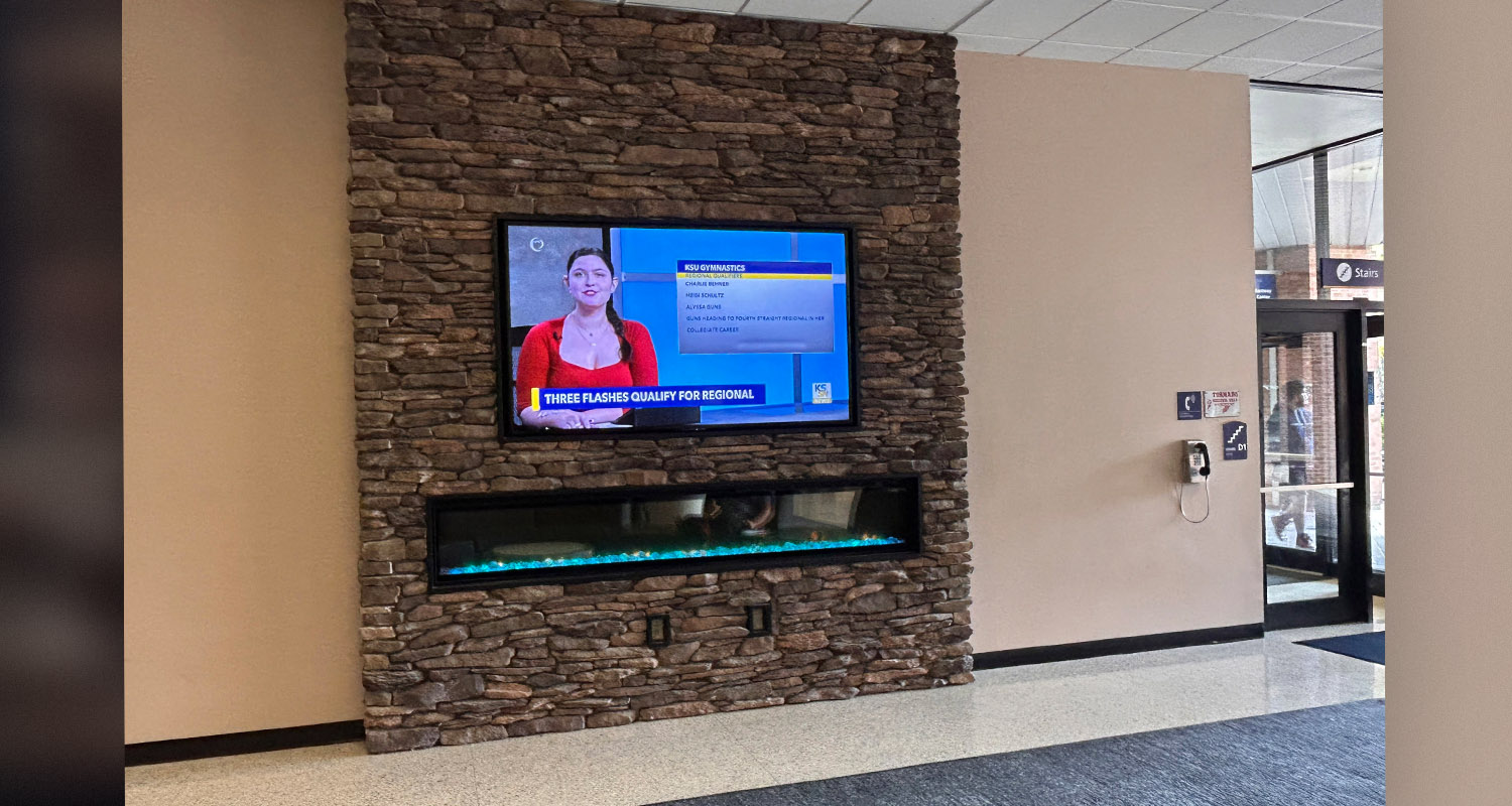 Large screen above fireplace in student center with KSTV news showing on it