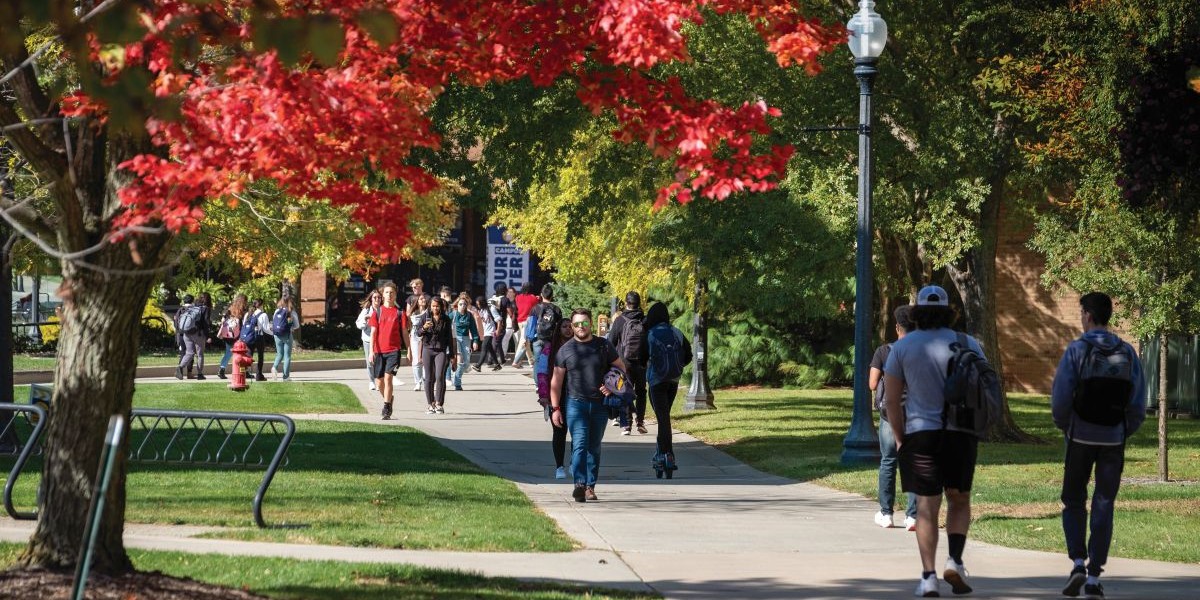 Students walk across campus past trees that display a variety of fall colors.