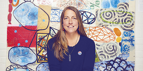Portrait of Liz Maugans in front of her artwork.