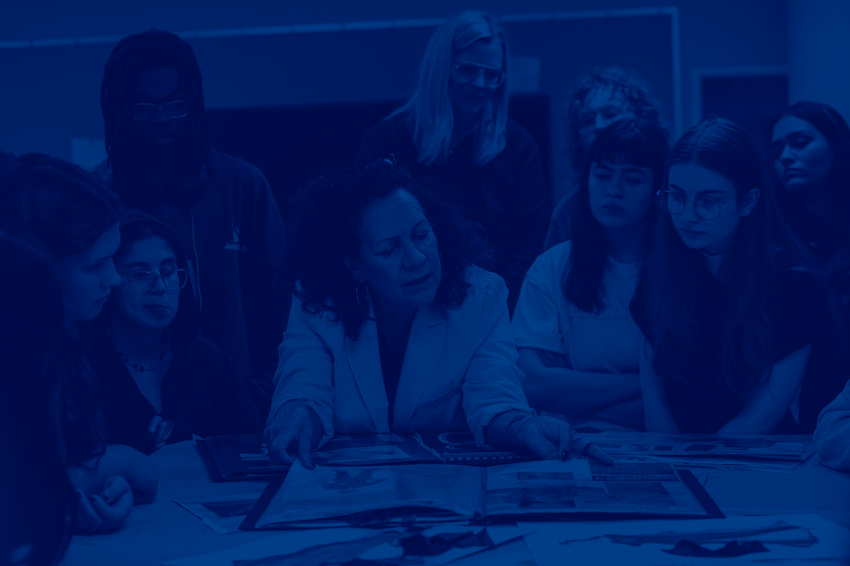 A professor critiques fashion designs guiding focused students gathered around a studio table in the Rockwell Hall museum.	