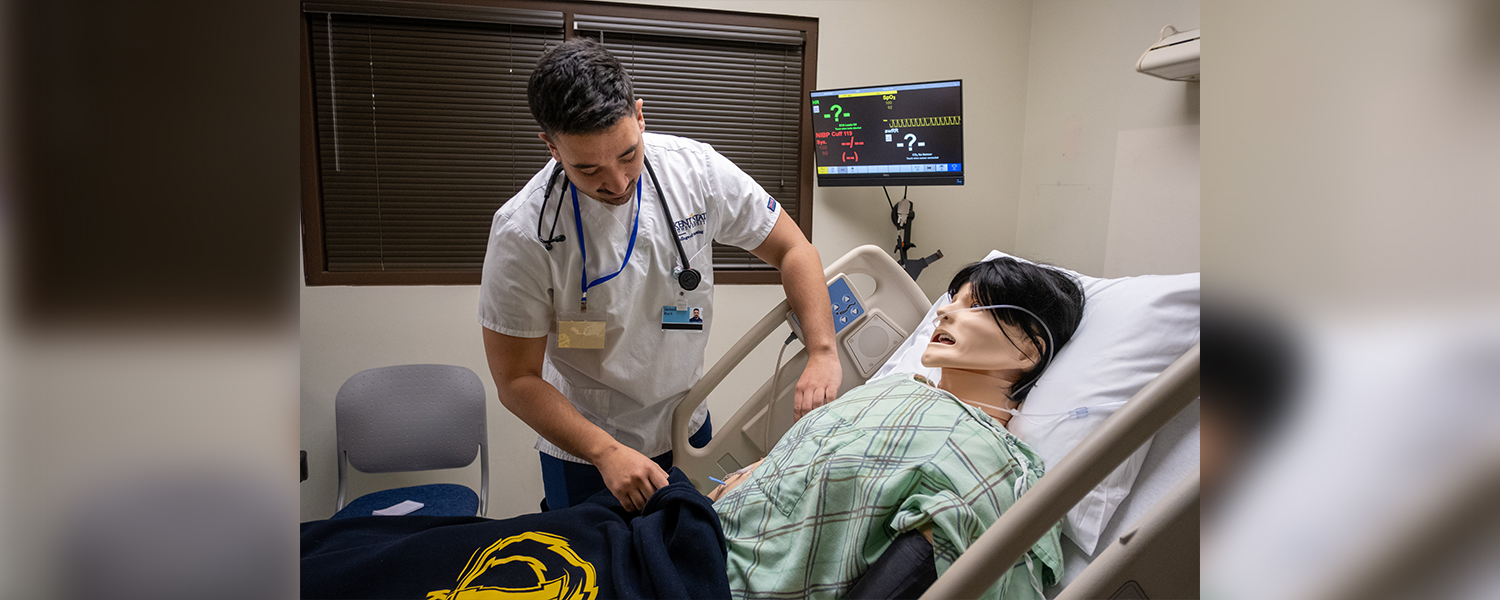 Male nursing student practicing in the simulation lab on a nursing manikin.