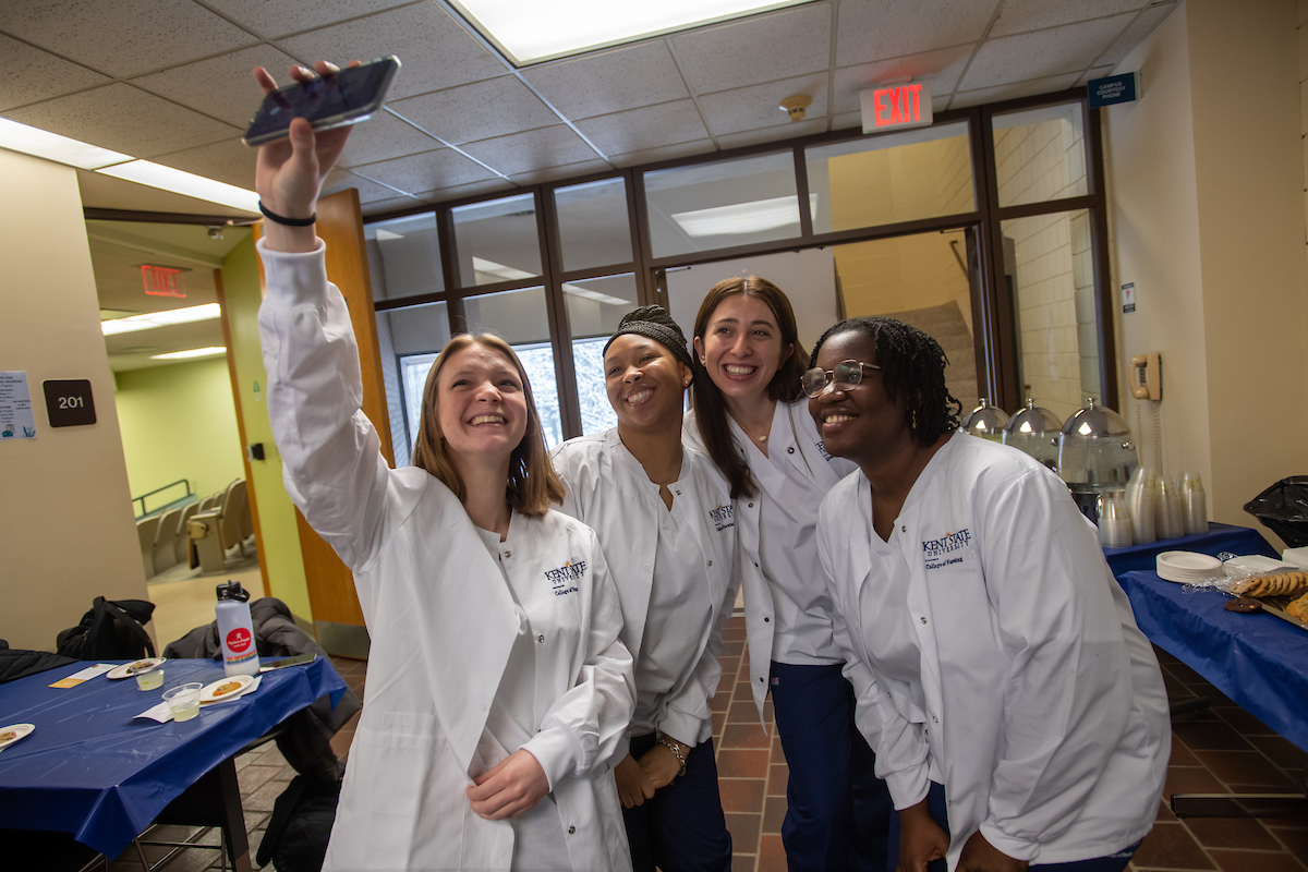 Four MŮ nursing students dressed in white coats taking a selfie. 