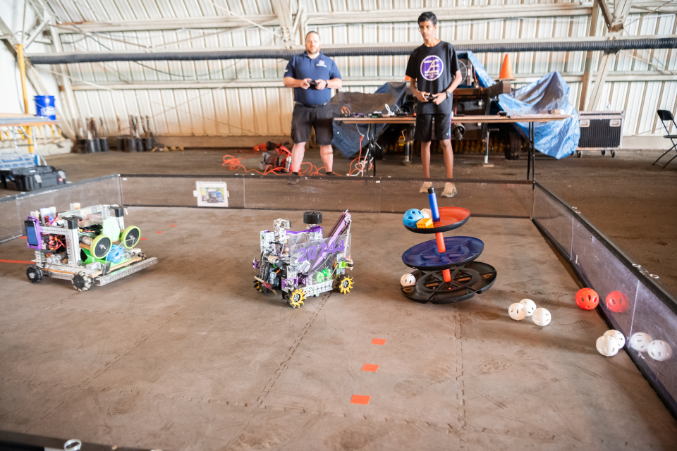Two students control two battle robots against each other in a low arena