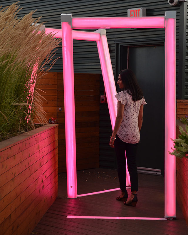 Scott Goss illuminated sculpture made of light-up tubing on a rooftop garden. A woman is standing inside of it.