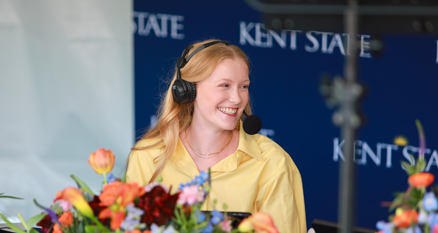 Student Sydney Brown poses with flowers while wearing a broadcast headset