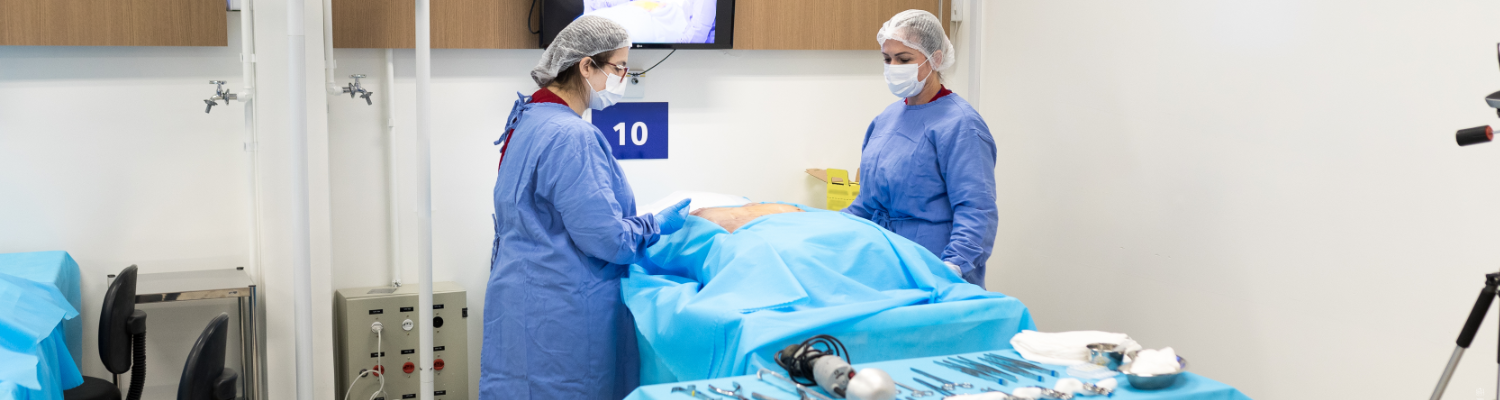 Two people in scrubs in an operating room exam an unseen patient