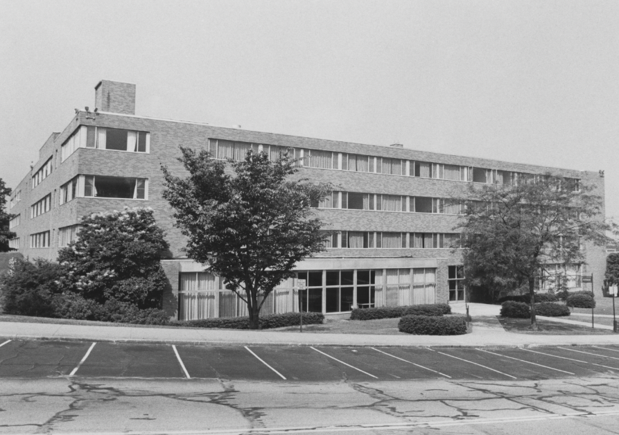 Black-and-white photograph of Kent State’s Verder Hall, viewed from the parking lot with trees framing the building.