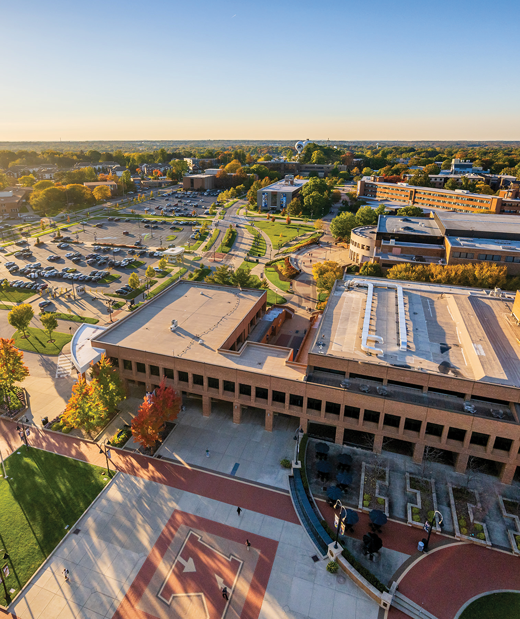 Aerial view of Kent State University’s campus on a sunny fall day, showing academic buildings, walkways, green spaces, and parking areas with colorful autumn trees.