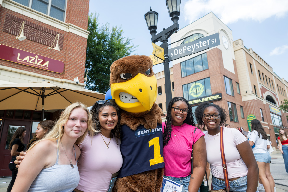 Four students posing with the �Ը������� mascot in downtown Kent.