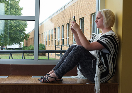 A student uses her cell phone. Student sitting in a window on their cellphone
