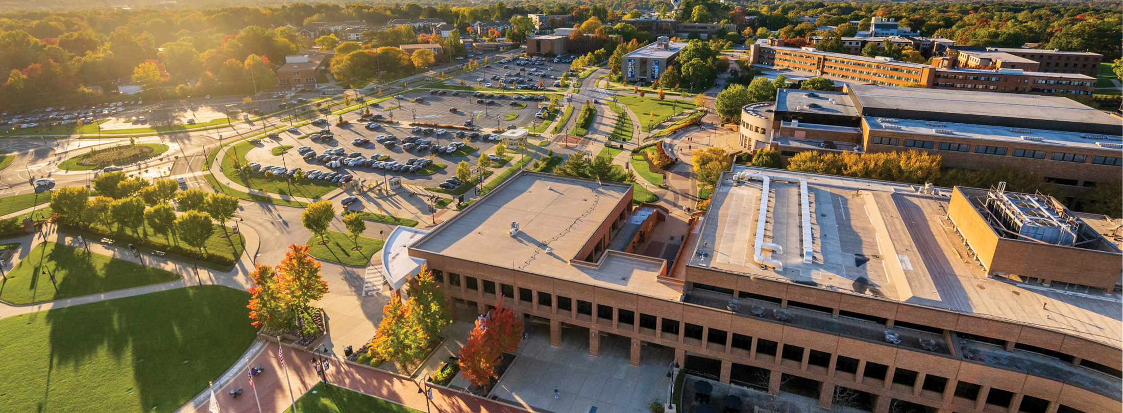 Aerial view of Kent State University’s campus on a sunny fall day, showing academic buildings, walkways, green spaces, and parking areas with colorful autumn trees.