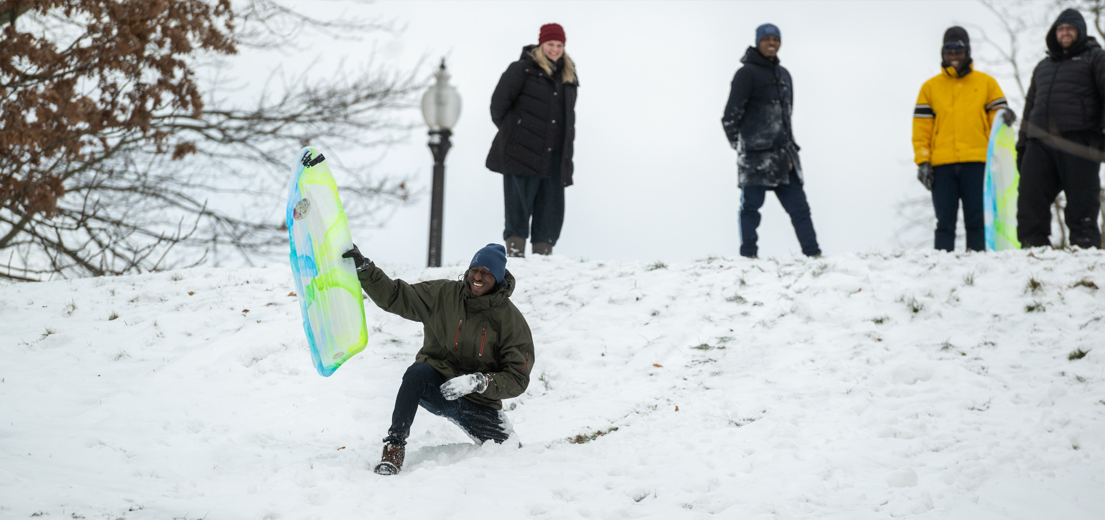 Kent State University students on a snowy day riding sleds down a hill.