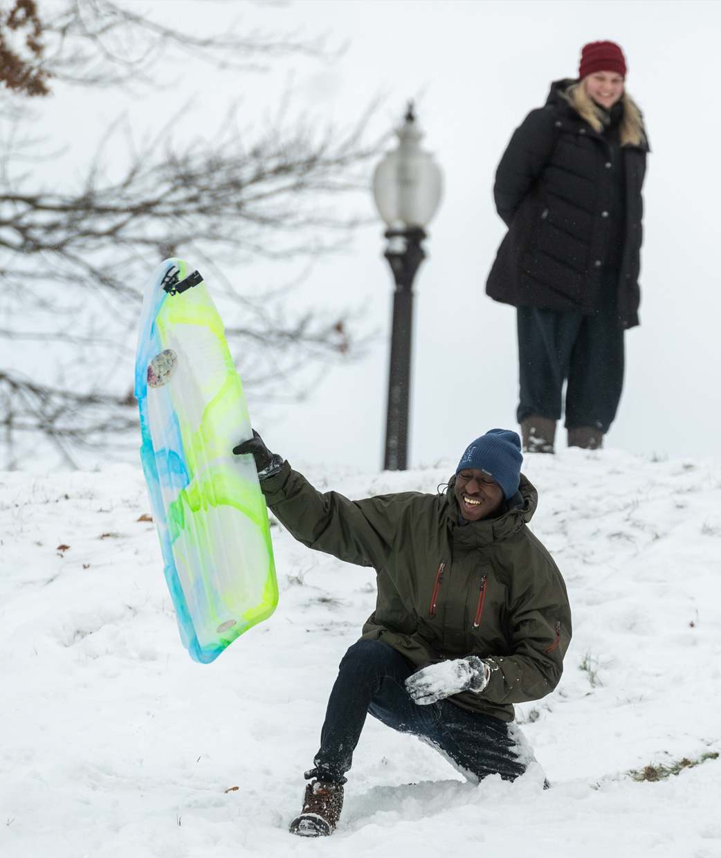 Kent State University students on a snowy day riding sleds down a hill.