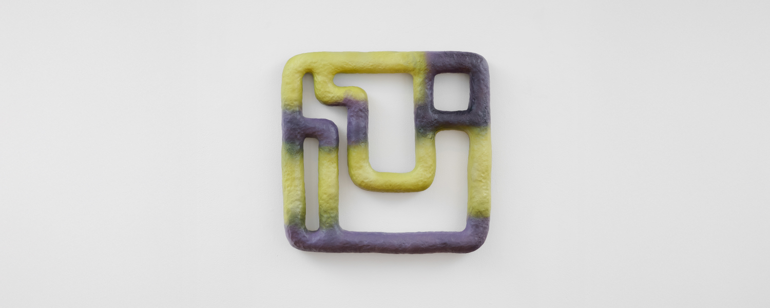 a purple and green geometric sculpture hanging on a gallery wall