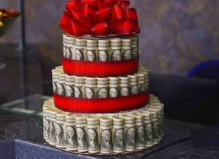 Rolled-up U.S. dollar bills arranged into a 3-tier "money cake" adorned with red ribbon