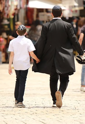 Man and child walk holding hands, wearing yamakas