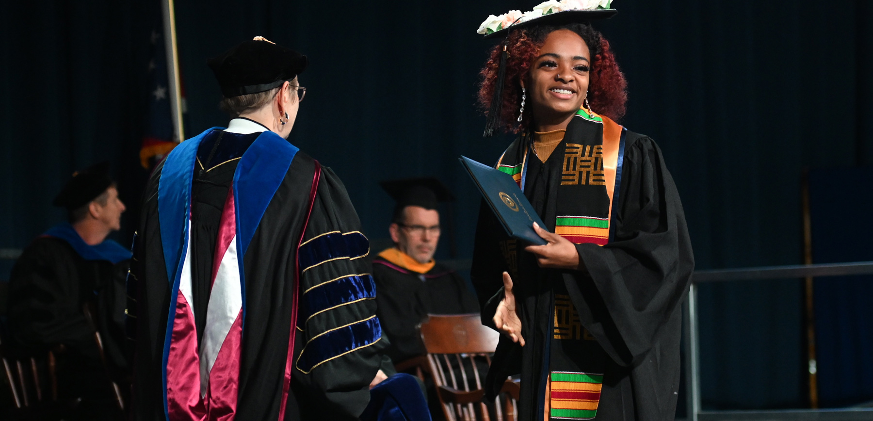 A new СƬƵ graduate smiles as she crosses the commencement stage holding her diploma.