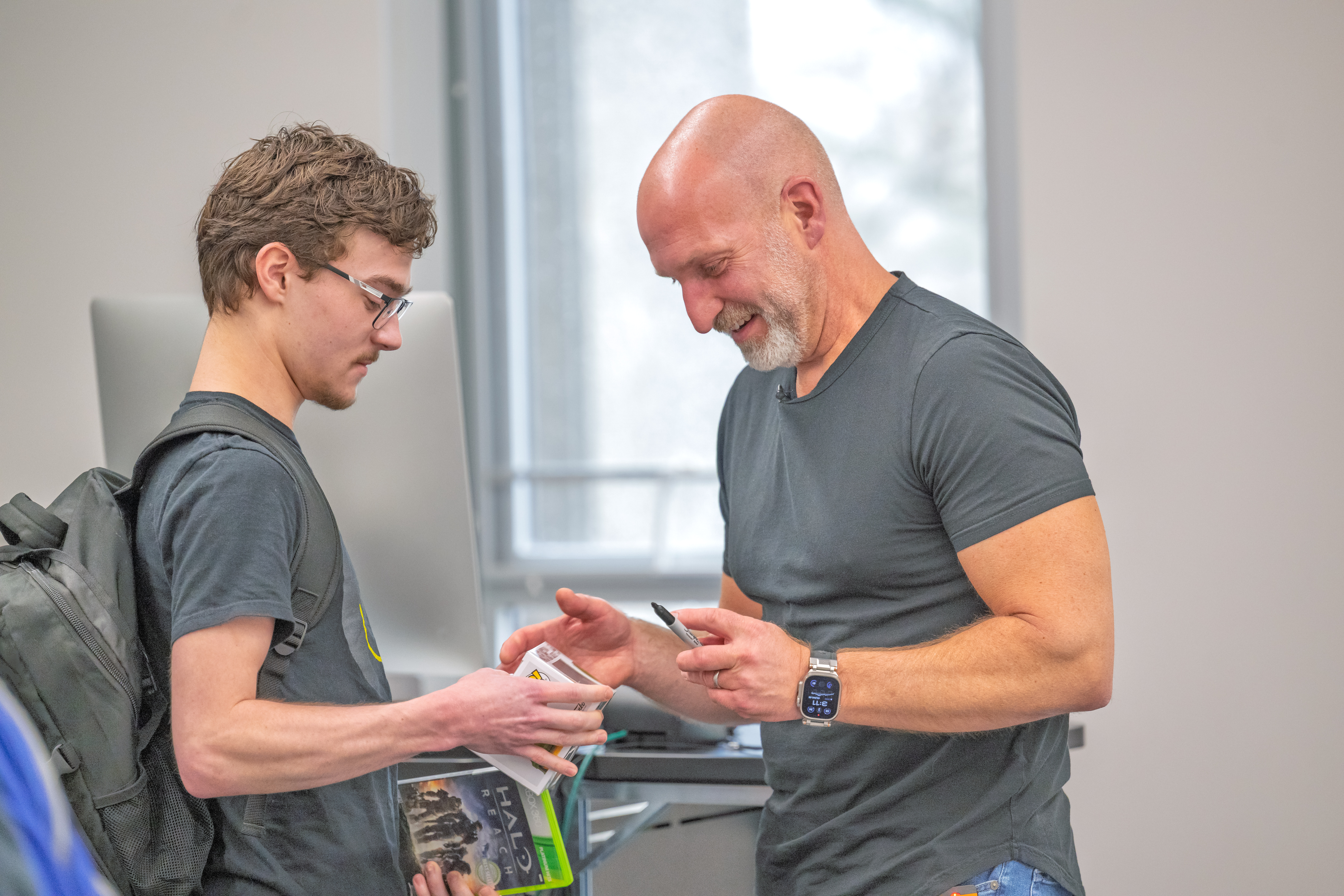 Marcus Lehto smiling as he signs Halo game cases for a Kent State VCD student holding several Halo titles.