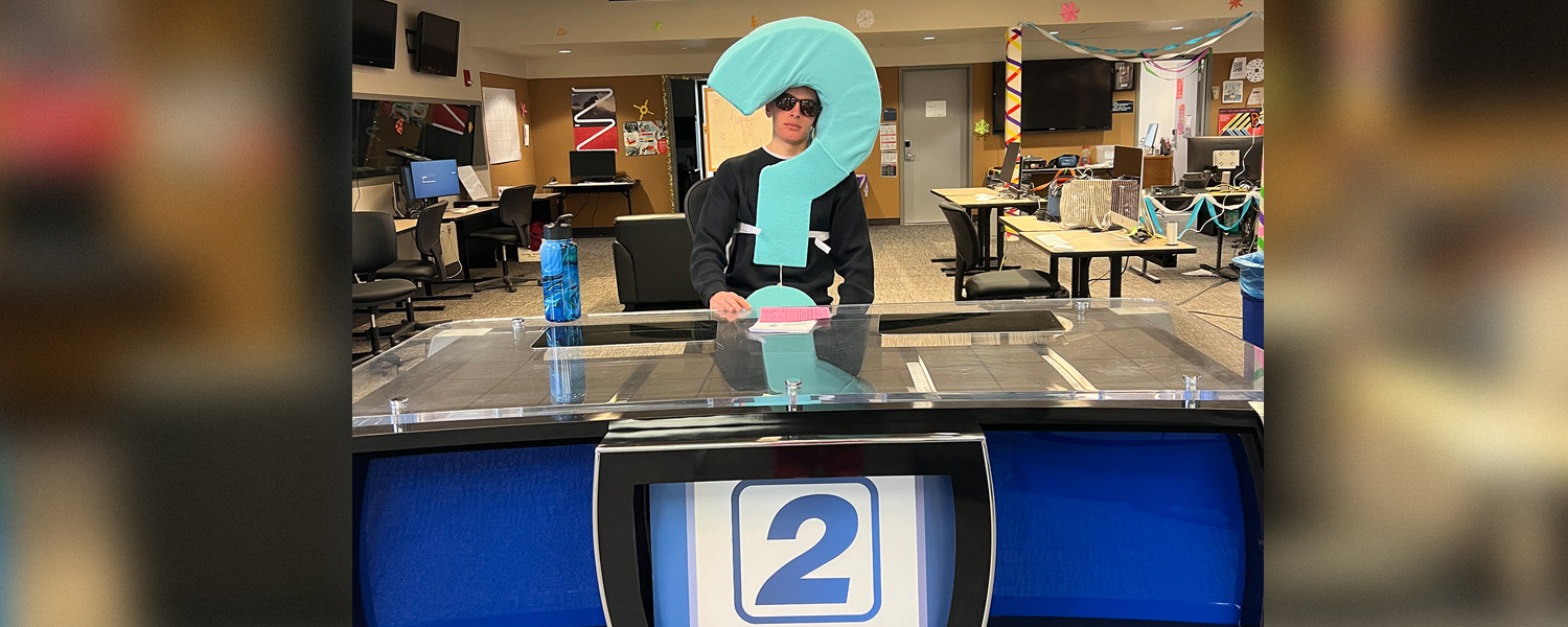 Student in Question Costume sitting at TV anchor desk