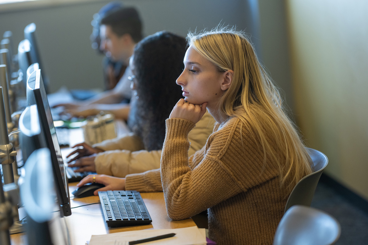 A student works at a desktop computer while other students use computers nearby.