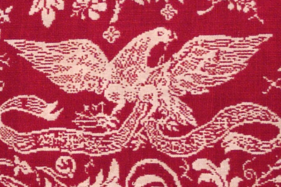 Detail of red fabric with a white eagle created with thread. 