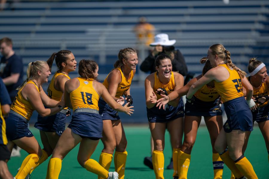 Members of Kent State’s field hockey team laugh and smile together on the field.