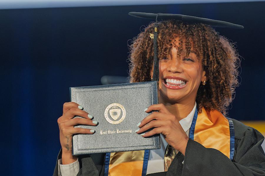 A new 5X���� graduate smiles as she holds her diploma up during the university’s summer 2025 commencement ceremony. (Photo credit: Rami Daud, 5X����)