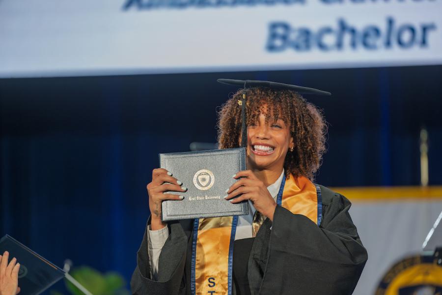 A new Kent State University graduate smiles as she holds her diploma up during the university’s summer 2025 commencement ceremony. (Photo credit: Rami Daud, Kent State University)