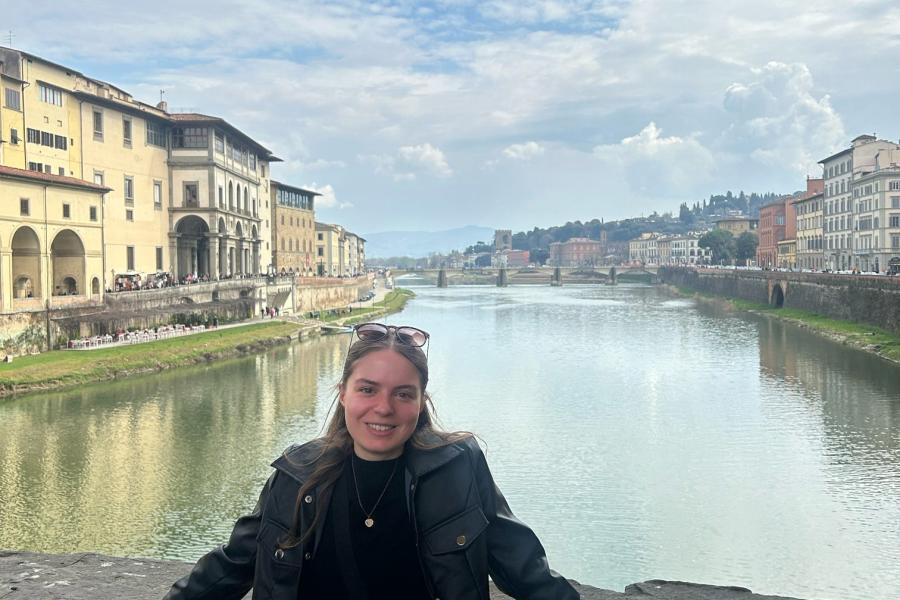 A student poses for a photo on a bridge with the Arno River in Florence, Italy behind them.