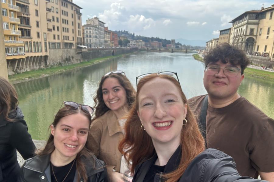 A group of students take a selfie with the Arno River in Florence, Italy behind them.
