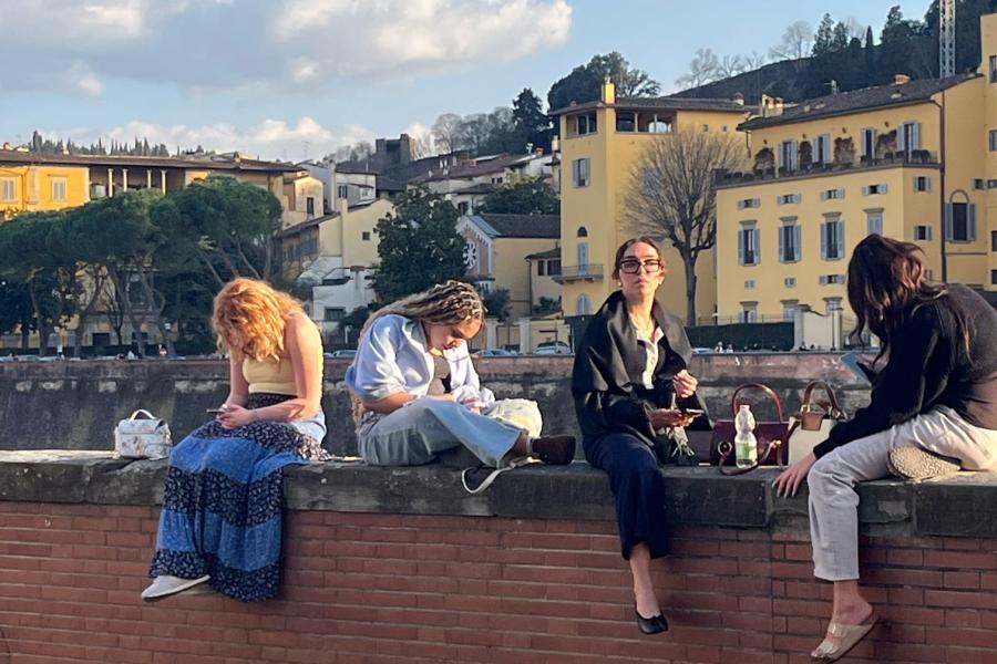 Four Exploratory students sit on top of a ledge overlooking the Arno River in Florence, Italy.