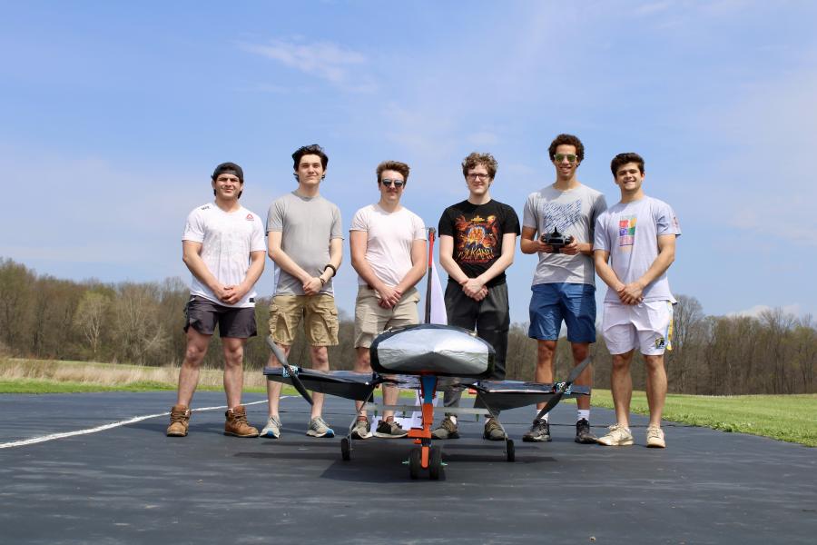 2026 Design, Build, Fly team consisting of six male college students standing on the runway behind their finished aircraft