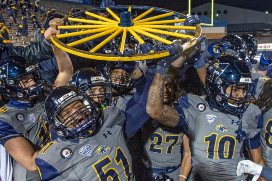 a group of football players hold up a yellow wagon wheel in victory.