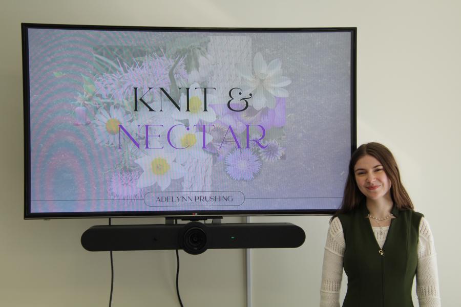 Adelynn Prushing poses for a photo in front of a TV screen displaying her brand logo.