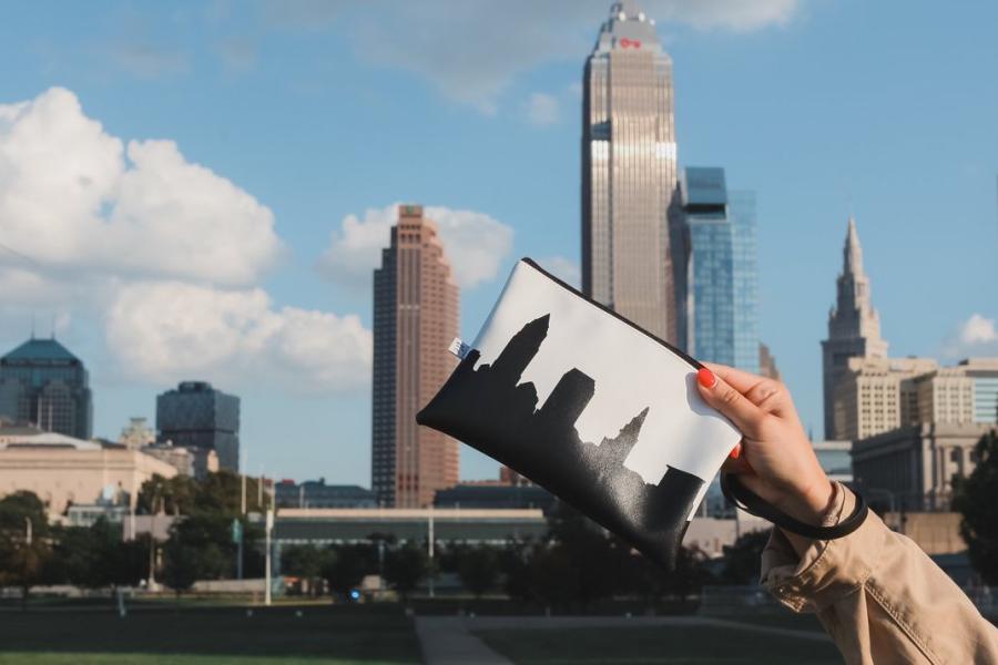 Anne Johnson holds up her Cleveland Skyline clutch in front of the Cleveland skyline.