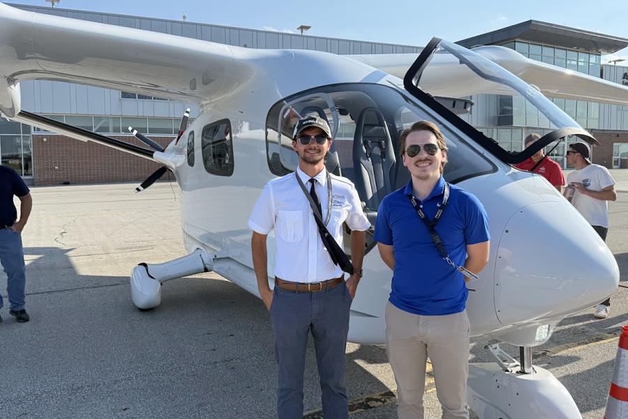 Two student pilots stand next to a modern single-engine aircraft outdoors.